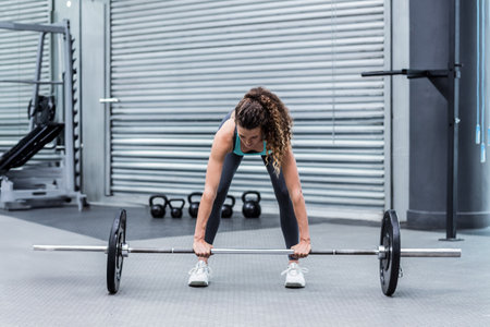 Barbell resting on flooring in strength zone with kettlebells leaning against metal shutter wall. Fitness, strength, training, gym, athletic, power, determinationの写真素材