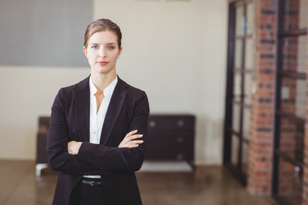 Businesswoman standing with arms crossed in office lobby showing bench seating and glass partition....