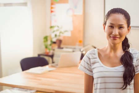 Asian woman standing at wooden desk in bright workspace using open laptop and notebooks, copy space. Productivity, innovation, minimalist, modern, professional, workspace, tranquilityの写真素材