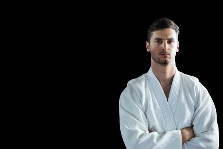 Adult male martial artist standing with crossed arms in studio wearing white gi, copy space. Athlete, discipline, strength, focus, minimalism, professionalism, trainingの写真素材