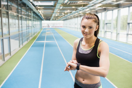 Athletic woman in sportswear checking smartwatch on right track in hall by glass wall, copy space. Fitness, infrastructure, modern, activity, sport, leisure, performanceの写真素材