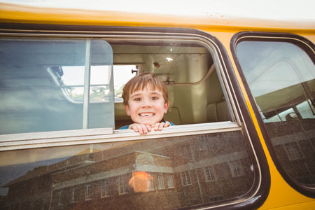 Boy leaning out of lowered window on yellow school bus on street, gripping window frame. Playground, transportation, adventure, childhood, outdoor, cheerful, urbanの写真素材