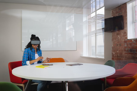 Staff wearing virtual reality headset is using yellow notebook and pen with tablet in meeting room. Futuristic, technology, innovation, collaboration, corporate, modern, creativeの写真素材