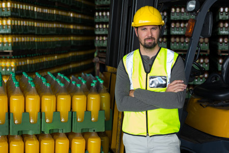 Male worker leaning against forklift wearing reflective vest in depot with juice crates, copy space....