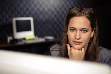 Adult female professional leaning on desk gazing at monitor with foam acoustic panels, copy space....