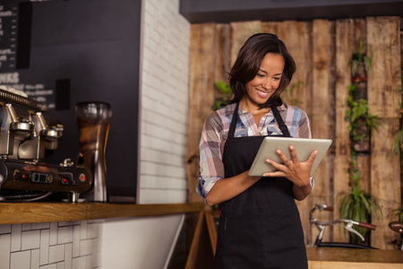 Asian woman barista wearing apron using tablet at tile counter near espresso and plants, copy space. Cafe, hospitality, interior design, modern, lifestyle, craftsmanship, digitalの写真素材