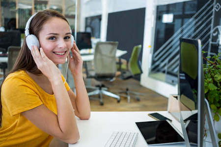 Adjusting over-ear headphones while sitting at desk in workspace with computer and smartphone....