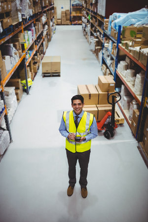 Male warehouse worker in safety vest scanning boxes in warehouse aisle with scanner and pallet jack. Industrial, logistics, organization, inventory, distribution, transportation, efficiencyの写真素材