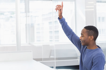 African American man raising hand while sitting at desk in office with glass partition, copy space. Professional, modern, collaborative, educational, corporate, minimalistic, innovativeの写真素材