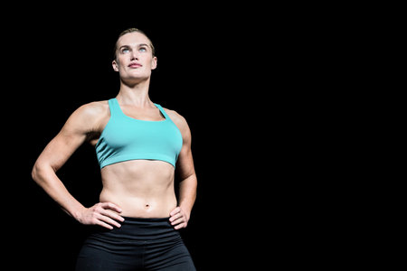 Female athlete posing confidently against black studio backdrop, showcasing sports bra and leggings. Fitness, empowerment, strength, determination, vitality, athleticism, motivationの写真素材