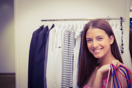 Woman in twenties smiling in clothing store holding colorful shopping bags on shoulder, copy space. Fashion, retail, storefront, style, casual, consumer, accessoriesの写真素材