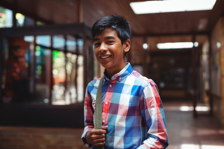 Asian teenage student smiling in school hallway holding shoulder bag strap by artwork, glass cases. Youth, education, academic, architecture, modern, vibrant, casualの写真素材