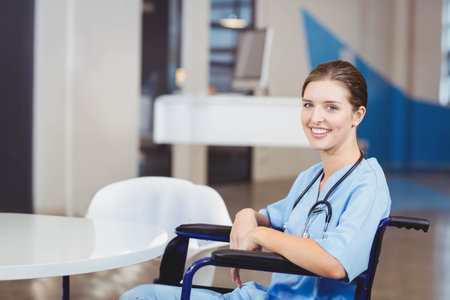 Female nurse in scrubs smiling while sitting in wheelchair at reception desk with stethoscope. Healthcare, medical, professional, approachable, modern, support, clinicの写真素材