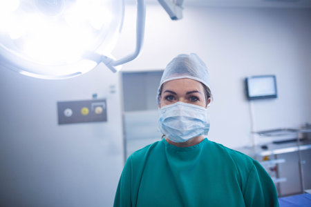 Female medical professional wearing surgical cap and mask adjusting control panel in operating room....
