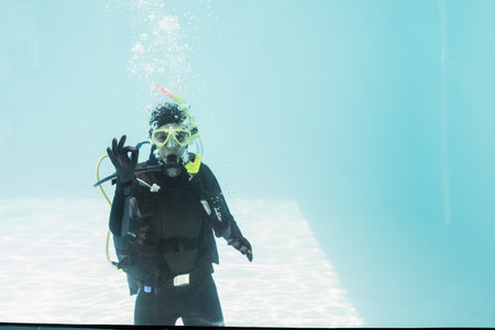 Scuba diver wearing yellow dive mask and scuba tank floating in clear pool water, bubbles rising....
