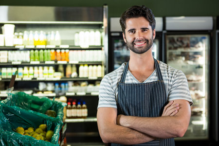 Male clerk wearing striped apron sorting yellow pears in grocery store by fridge cases, copy space. Retail, freshness, merchandising, uniform, industry, customer service, vibrantの写真素材