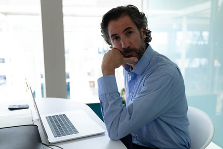 Senior male professional leaning on hand while using laptop at modern office desk, copy space....