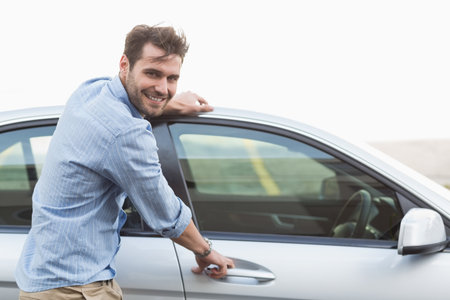 Man standing beside silver sedan on road pulling driver's door handle and checking wristwatch....