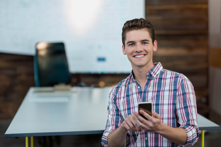 Smiling man holding smartphone in conference room near conference table and screen, copy space. Professional, corporate, modern, energetic, business, communicative, contemporaryの写真素材