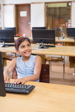 Indian girl child typing on keyboard at school computer lab with desktop monitor and wooden desk....