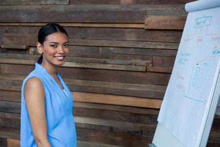 Asian woman presenting growth graphs on flip chart at office with wooden wall, copy space. Professional, collaboration, modern, analytics, corporate, motivational, strategicの写真素材