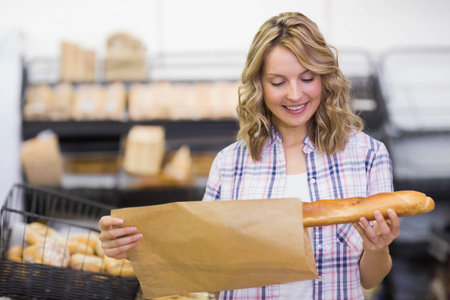 Female customer selecting fresh baguette and packing into brown paper bag at bakery display. Bakery, artisan, rustic, fresh, retail, shopping, domesticの写真素材