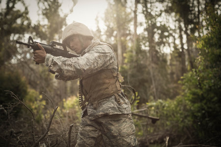 Soldier wearing tactical vest and helmet, moving through dense woodland, scanning ahead with rifle. Military, reconnaissance, stealth, camouflage, outdoor, strategic, adventureの写真素材
