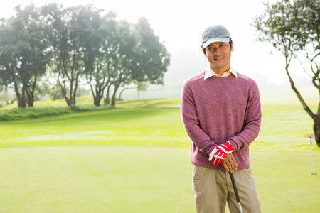 Mid adult Japanese man standing on putting green holding golf club near flagstick, copy space. Sport, leisure, outdoor, recreation, elegance, tranquility, natureの写真素材