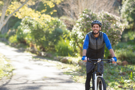 Male cyclist riding mountain bike along sunlit paved park trail with helmet and gloves, copy space....