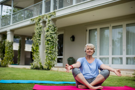 Woman meditating in activewear on pink yoga mat beside blue yoga mat on lawn, copy space. Outdoor, wellness, tranquility, harmony, leisure, serenity, re-creationの写真素材