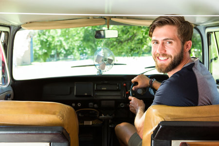 Man sitting in vintage camper van driver seat adjusting clip-on fan while looking back, copy space....