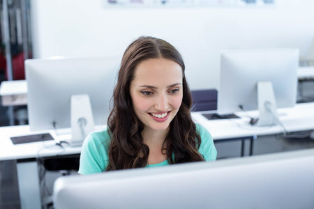Woman in mid-20s smiling while sitting at computer lab workstation using monitor and keyboard....