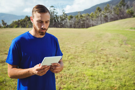Man standing in grassy meadow holding white tablet and looking down at screen, copy space. Nature,...