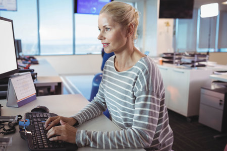 Coworkers typing on keyboard while checking monitor in office with large windows near desk phone....