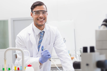 Male scientist in lab coat pipetting liquids into test tube rack with micropipette at lab bench. Scientist, laboratory, research, experimentation, chemistry, innovation, scientificの写真素材