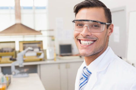 Man wearing lab coat, striped tie and safety goggles examining sample under microscope on lab bench. Scientist, laboratory, research, innovation, experimentation, equipment, scientificの写真素材