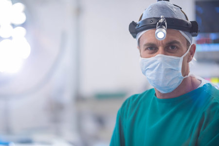 Senior male surgeon adjusting surgical headlight in operating room with monitors, lamps, copy space. Medical, healthcare, operation, clinical, professional, sterile, precisionの写真素材