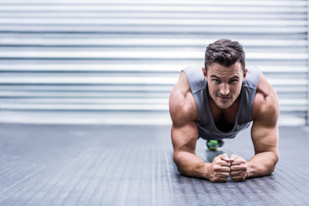 Man holding forearm plank on rubber gym floor against corrugated metal shutter wall, copy space. Fitness, strength, endurance, gym, training, workout, motionの写真素材