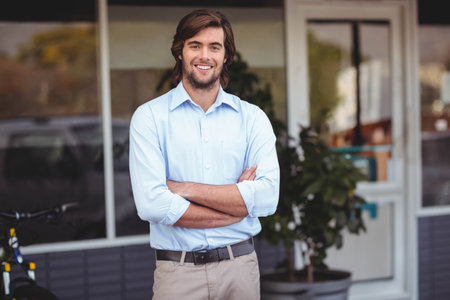 Man standing cross-armed smiling outside shop with glass door, windows, bicycle, potted plant. Urban, modern, professional, casual, exterior, storefront, contemporaryの写真素材