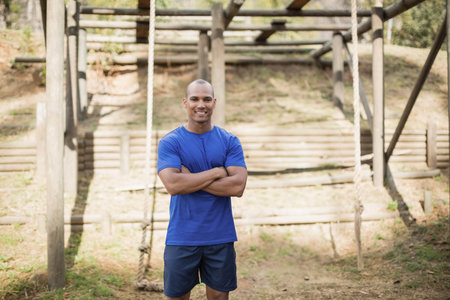 African American man wearing athletic wear standing at park obstacle course with logs and ropes....