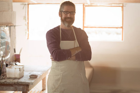 Adult male craftsman standing at workshop wearing stained apron mixing paint in bowl on workbench. Artisan, studio, creative, craftsmanship, rustic, handmade, renovationの写真素材