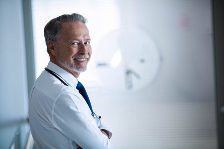 Senior male doctor standing in clinic hallway wearing stethoscope and necktie, copy space. Professional, healthcare, modern, sanitation, consultation, examination, clinicの写真素材