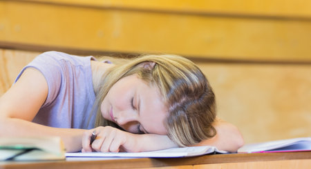 Female teenager resting head on open notebooks and textbooks while holding pen at classroom desk. Student, education, studying, classroom, youthful, academic, concentrationの写真素材
