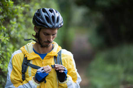 Man standing on wooded trail adjusting backpack strap while wearing cycling helmet and windbreaker. Adventure, outdoor, nature, exploration, fitness, activity, environmentの写真素材