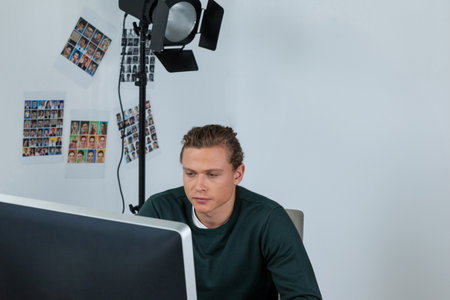 Desktop monitor shining on desk under studio spotlight with headshots on wall, copy space. Professional, creative, modern, office, workspace, focused, artisticの写真素材