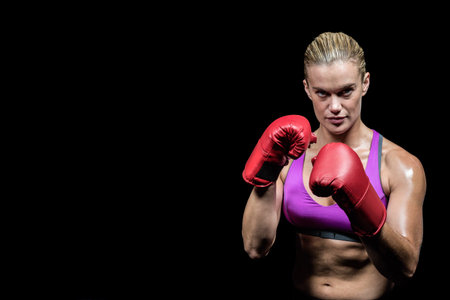 Woman posing in guard stance in studio with sports bra and red boxing gloves, copy space. Strength, determination, empowerment, athleticism, fitness, performance, resilienceの写真素材
