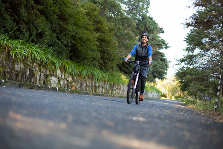 Male wearing bike helmet and backpack riding bicycle along rural road beside stone wall. Adventure,...