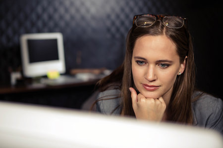 Woman leaning in blazer gazing at monitor with sticky note on office desk, copy space. Professional,...