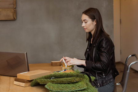 Woman wearing leather jacket sitting at coworking table eating salad near open laptop, copy space....
