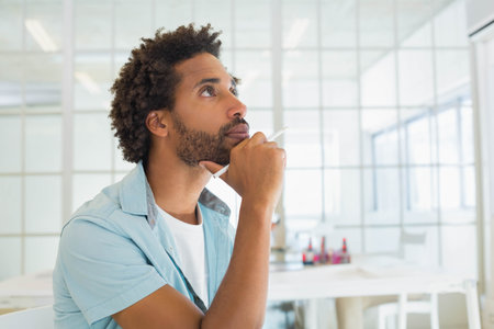 Mid adult African American man holding stylus pen, gazing upward at desk in office, copy space....